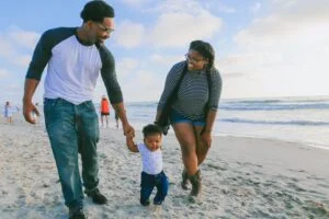 A Black family walks on the beach, smiling at each other