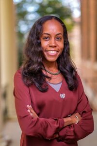 Dr. Nina Smith is a Black women with long black hair, wearing a burgundy long sleeve shirt, with her arms crossed